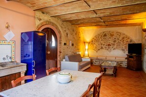 A kitchen with a blue refrigerator, a dining table with chairs, a stone wall, a sofa, and a television.