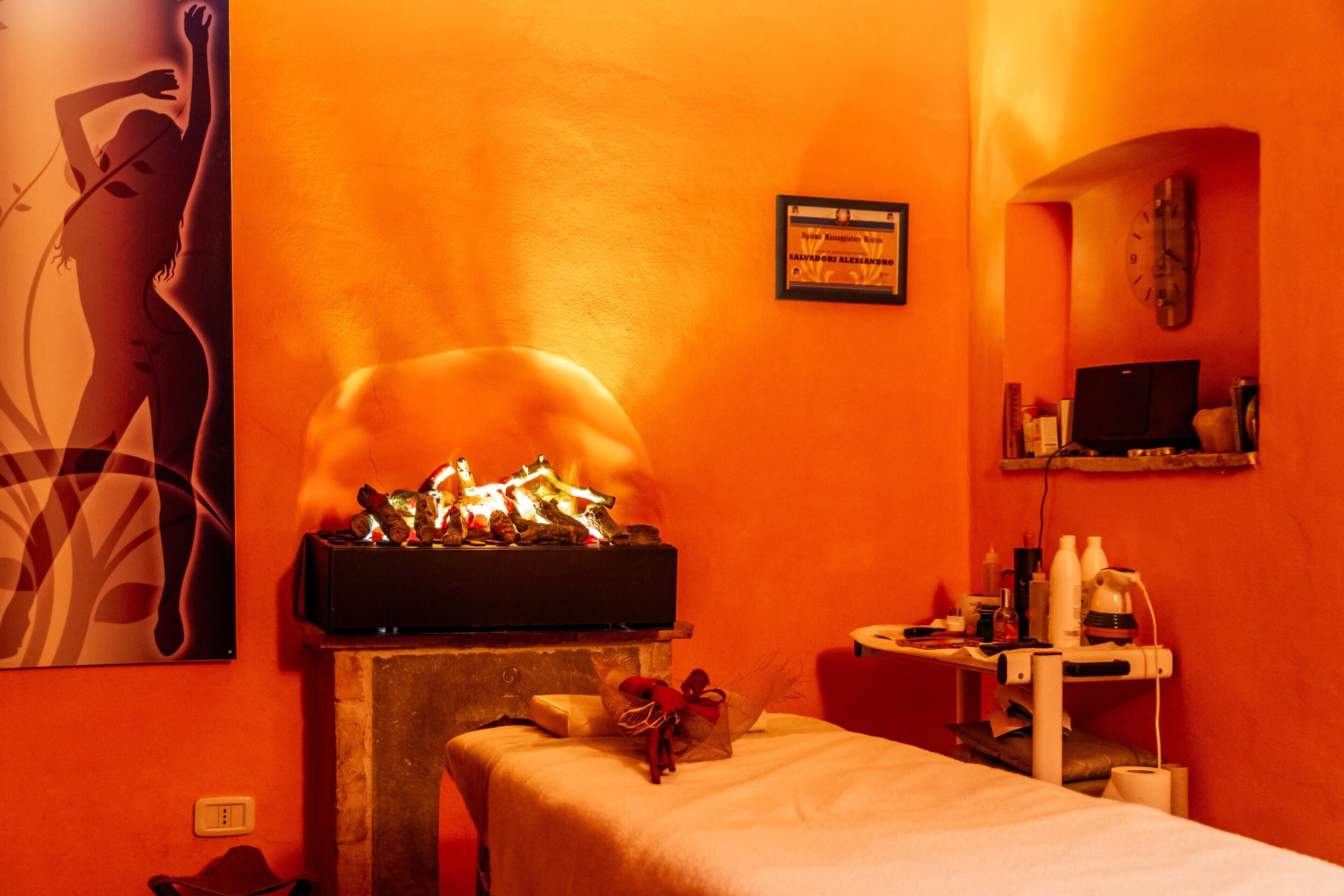 A room with a fireplace, a bed, a massage table, a clock, and a framed certificate on the wall.