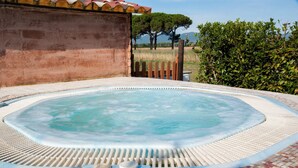Een hottub met betegelde rand, omgeven door een terras van bakstenen en een houten omheining.