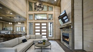 A spacious living area with a large sofa, a coffee table, and leather chairs. A fireplace is built into the wall, and a flat-screen TV is mounted above it. - NEW Cozy Lux Cabin! *VIEWS* Hot Tub,Wi-Fi-Sleeps 8 (Broken Bow)