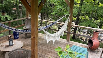 Een houten terras met een hangmat, een tafel met stoelen en een blauwe stoel.