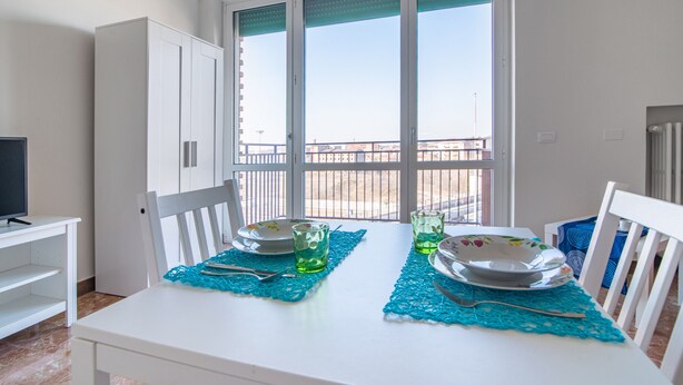 A dining area with a table set for two, a television on a stand, and a view of the outside balcony. - Casa Carolina (Pavia)