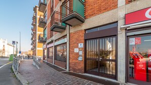 A brick building with a storefront, a gated entrance, and a sidewalk. - Casa Carolina (Pavia)