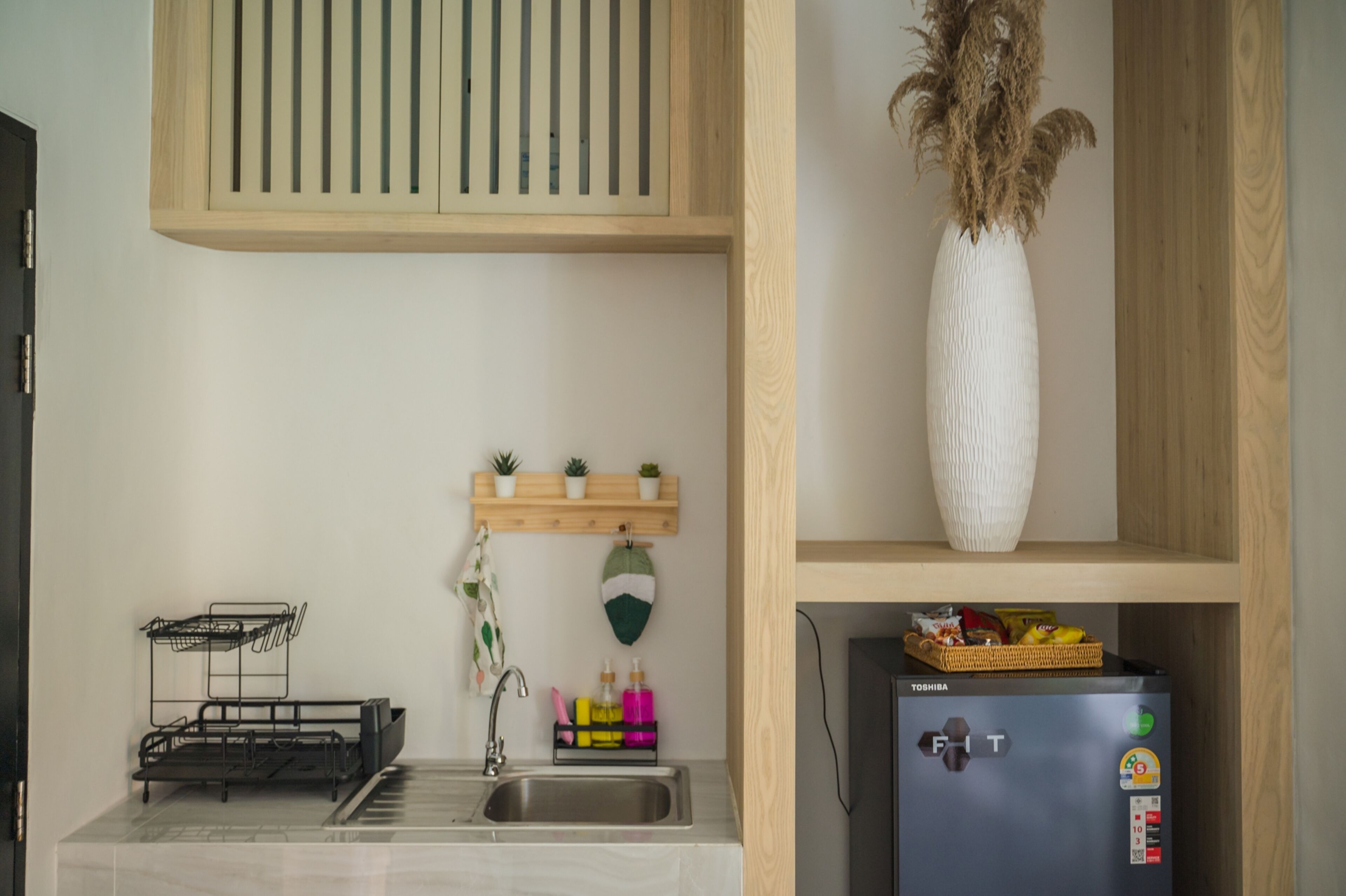 A compact kitchen with a built-in sink, a small refrigerator, and a shelf with potted plants.