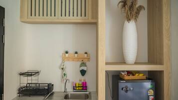 A compact kitchen with a built-in sink, a small refrigerator, and a shelf with potted plants.