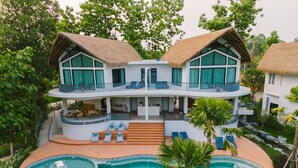 Un resort de dos pisos con piscina, mobiliario exterior y techo de paja.