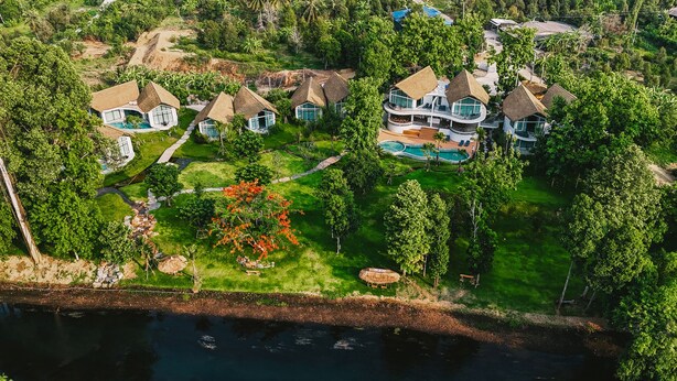 Vista aérea de un resort con varias cabañas de techo de paja, una gran piscina y abundante vegetación que rodea la propiedad.