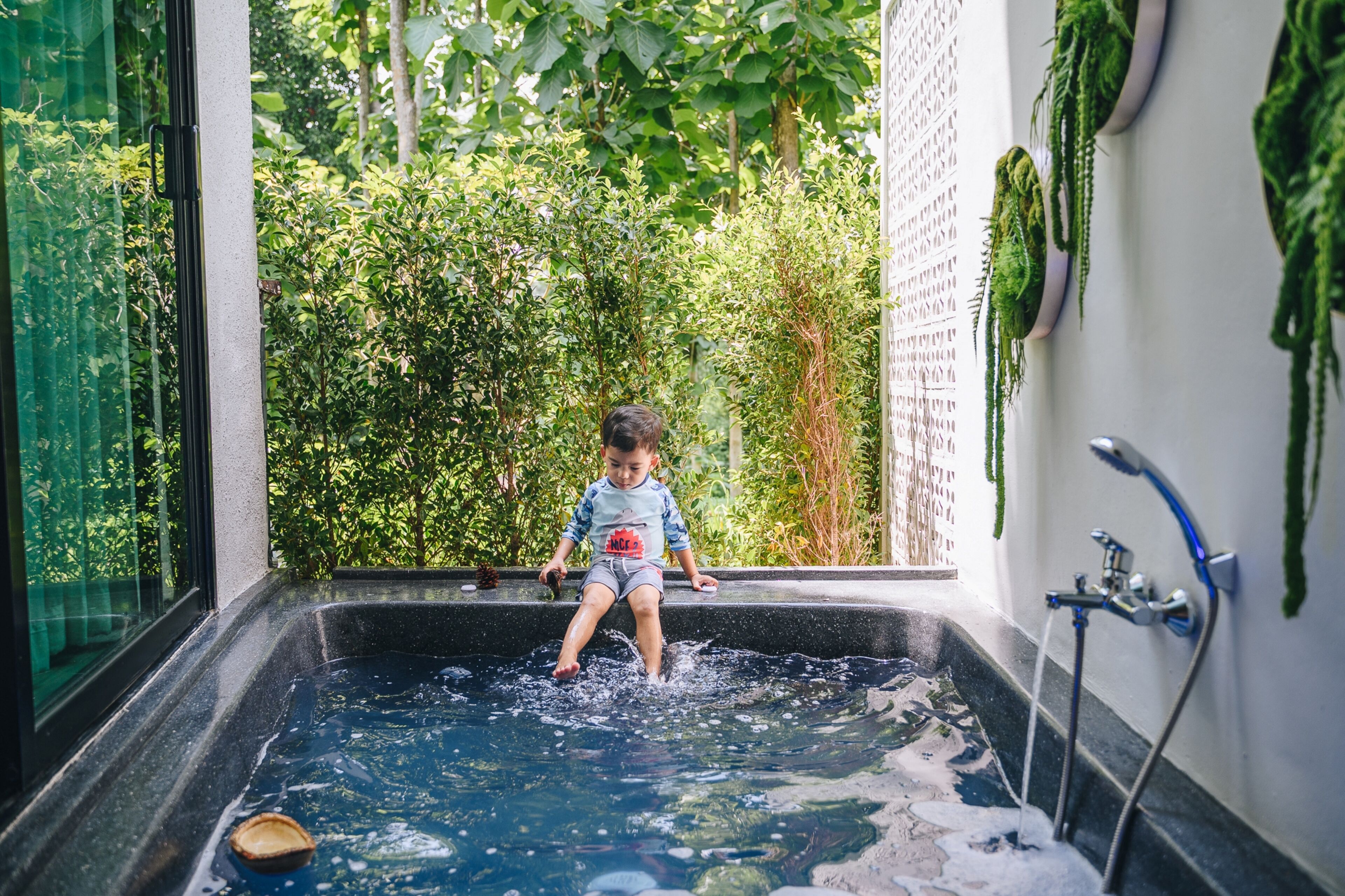 A child sitting in a bathtub with a view of lush greenery outside.