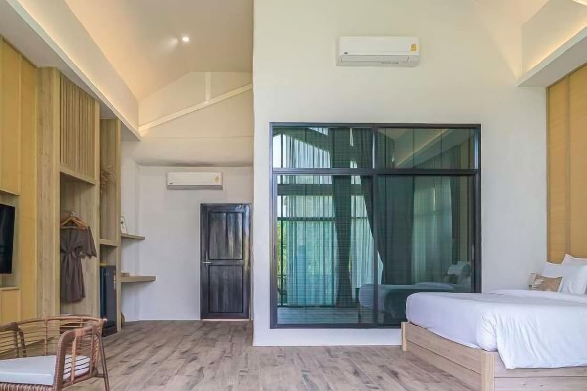 A modern hotel room with a bed, a seating area with chairs, a wardrobe, and a large window.