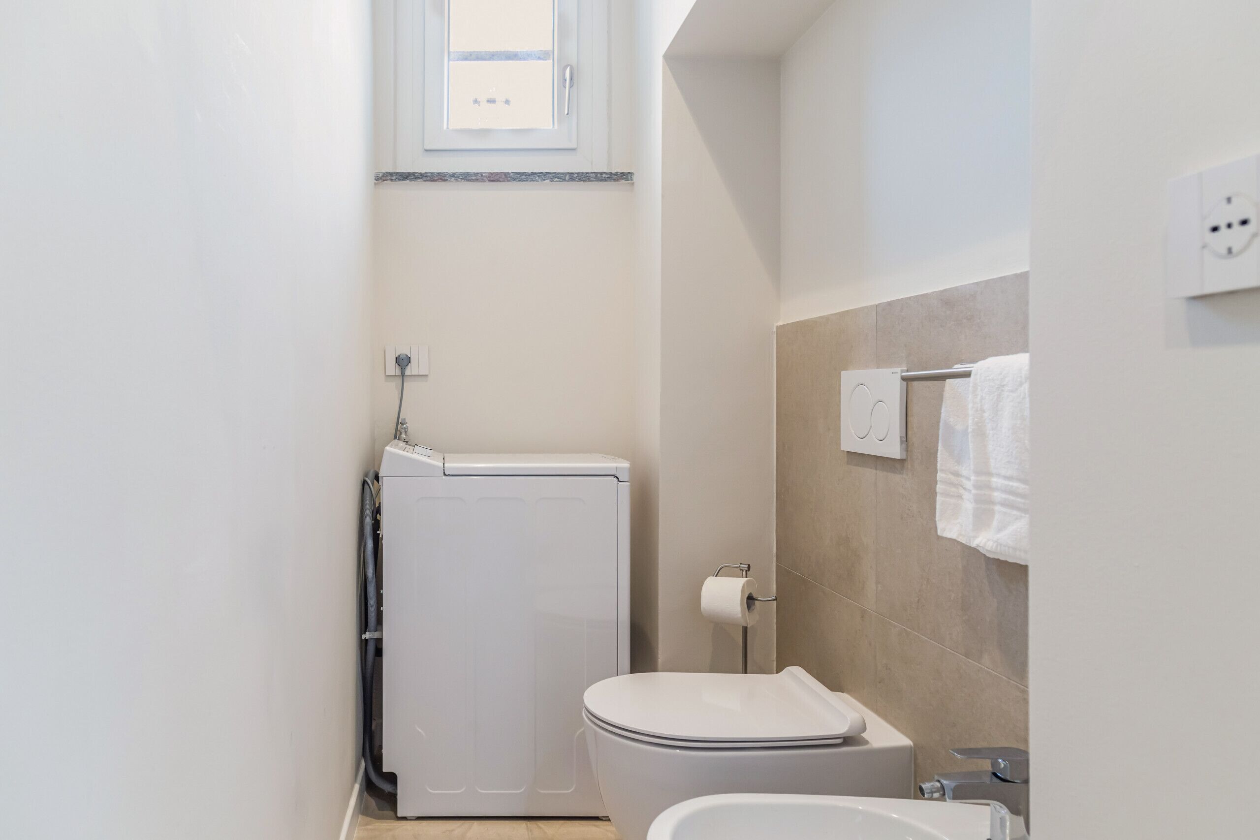 Een kleine badkamer met toilet, hygiëneschuimer en wastafel.