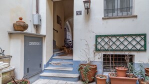 A narrow alleyway with steps leading to a door labeled "Contatori Gas." There are several potted plants along the path, and a window with a green lattice on the right. - VickyLù (Pavia)