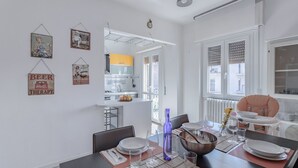 Un comedor con una mesa preparada para cuatro, una cocina al fondo y una trona para bebé.