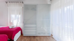 Un dormitorio con cama, armario y ventana con cortinas traslúcidas.