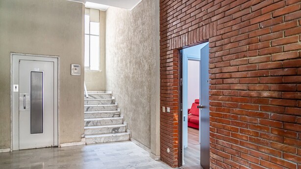 Un pasillo con una escalera de mármol, una puerta roja y una pared de ladrillo.