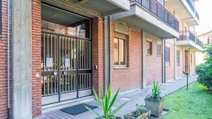 Un edificio de ladrillo con entrada porticada, plantas en macetas y un pequeño jardín.