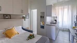 A modern hotel room with a bed, bedside table, and a small kitchenette. - Casa Elena (Pavia)