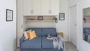 A modern living room with a blue sofa, white cabinets, a framed picture, and a small plant. - Casa Elena (Pavia)