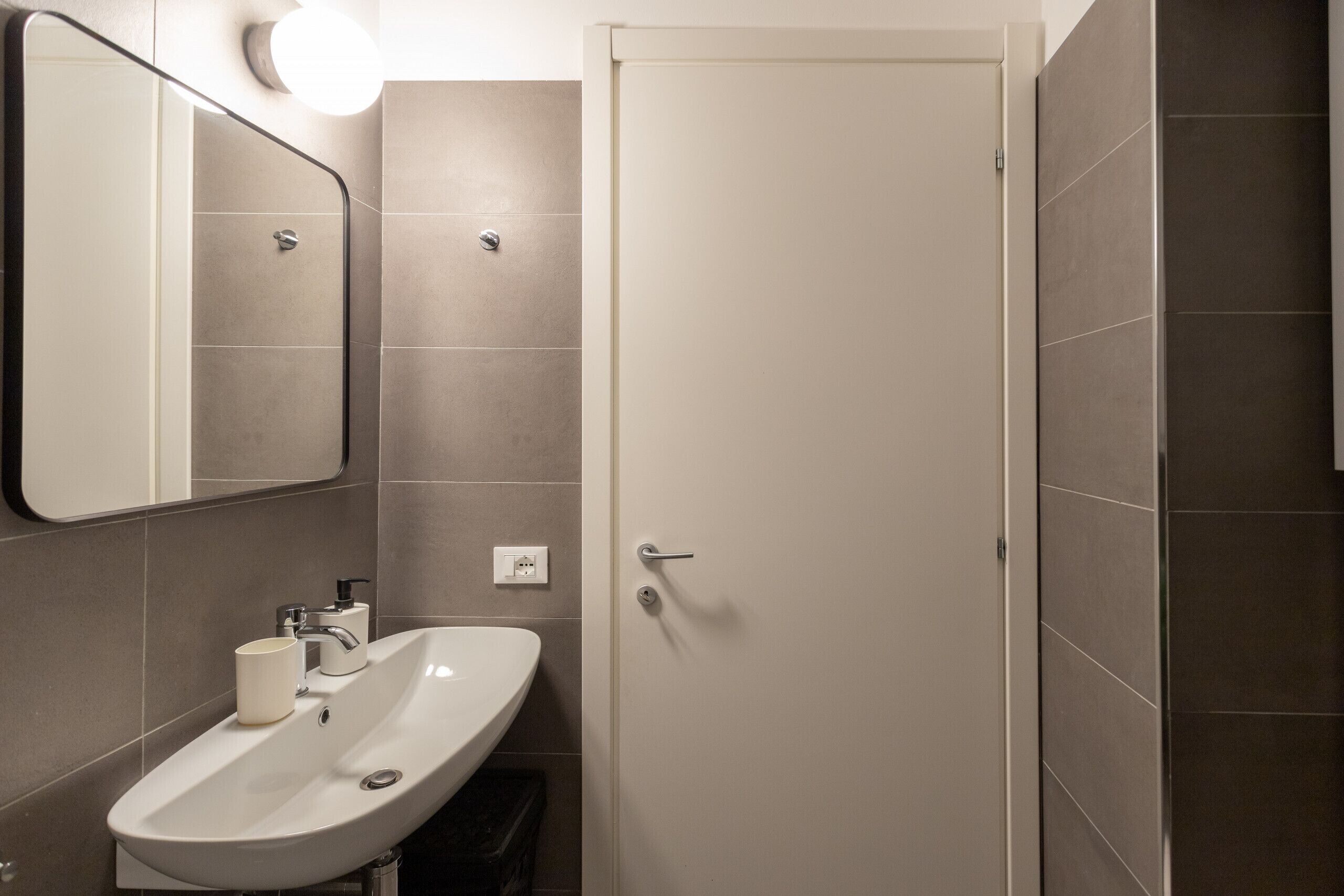 A bathroom with a white sink, mirror, and door.
