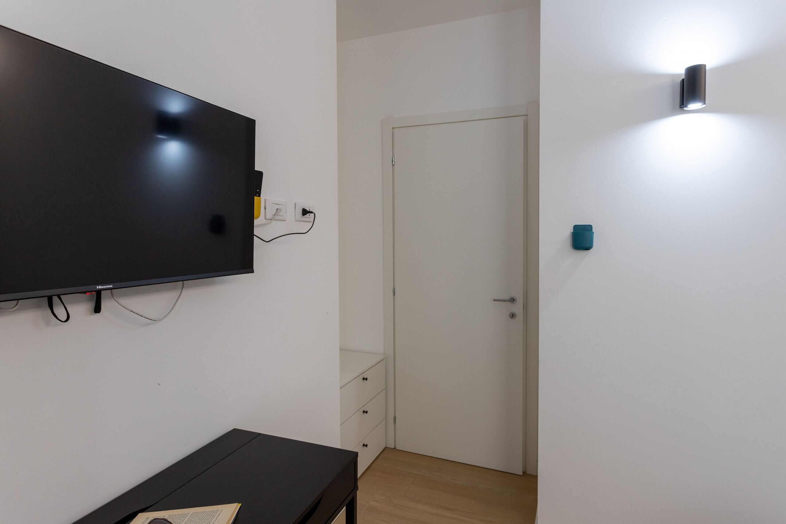 A room with a flat-screen TV mounted on the wall, a door, and a wall-mounted light fixture.