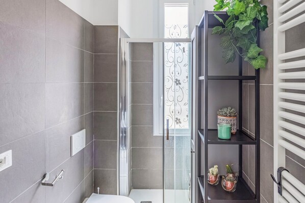 A modern bathroom with a glass shower enclosure, a white bathtub, and a shelf with potted plants.
