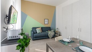Uma sala de estar moderna com um sofá, uma mesa de jantar posta para dois e uma televisão fixada na parede.