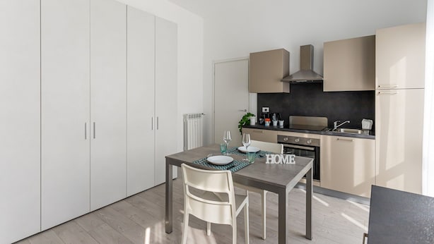 Uma cozinha moderna com armários brancos, bancada escura e área de refeições com mesa e cadeiras.