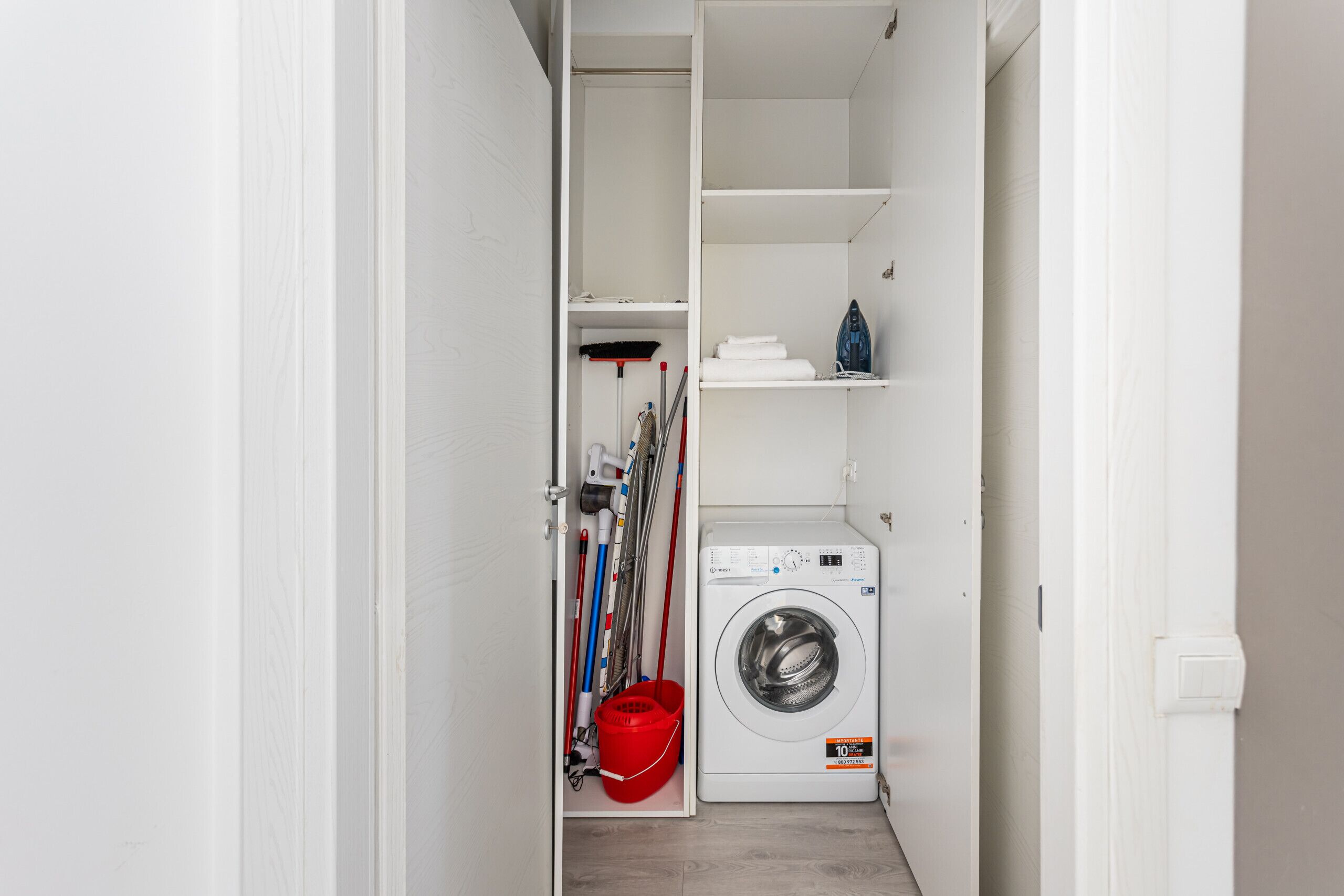 A laundry room with a washing machine, shelves, and cleaning supplies.