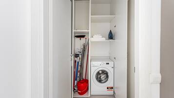 A laundry room with a washing machine, shelves, and cleaning supplies.