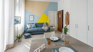Un saló modern amb un sofà blau, una taula de menjador preparada amb gots i plats, i un disseny de paret geomàtric.