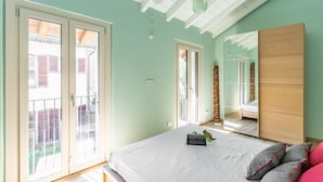A bedroom with a large bed, a wooden wardrobe, a mirror, and a sliding glass door leading to a balcony. - Casetta Cascina Rizzo (Pavia)