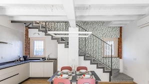 A dining area with a table set for four, a kitchen with white cabinets, a brick accent wall, and a staircase with a patterned railing. - Casetta Cascina Rizzo (Pavia)