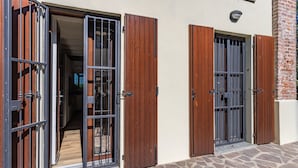 A building with two open wooden doors with metal bars, a stone-paved entrance, and a brick wall. - Casetta Cascina Rizzo (Pavia)