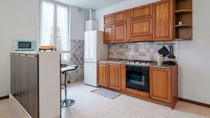 A compact kitchen with wooden cabinets, a microwave, a refrigerator, a stove, and a sink. - Via Cremona (Brescia)