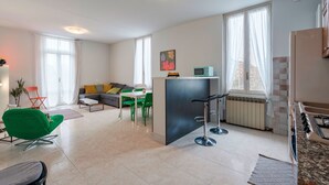 A modern apartment with a kitchen, dining area, and living room. It features a green chair, a sofa, and a small island with a bar stool. - Via Cremona (Brescia)