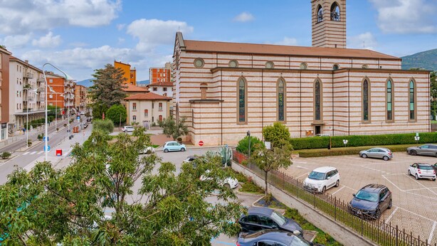 A church with a bell tower, parking lot, and surrounding buildings. - Via Cremona (Brescia)