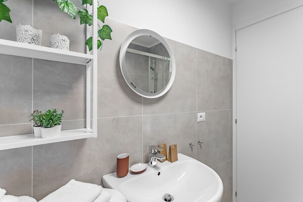 A modern bathroom with a white sink, a round mirror, and a shelf with decorative items.