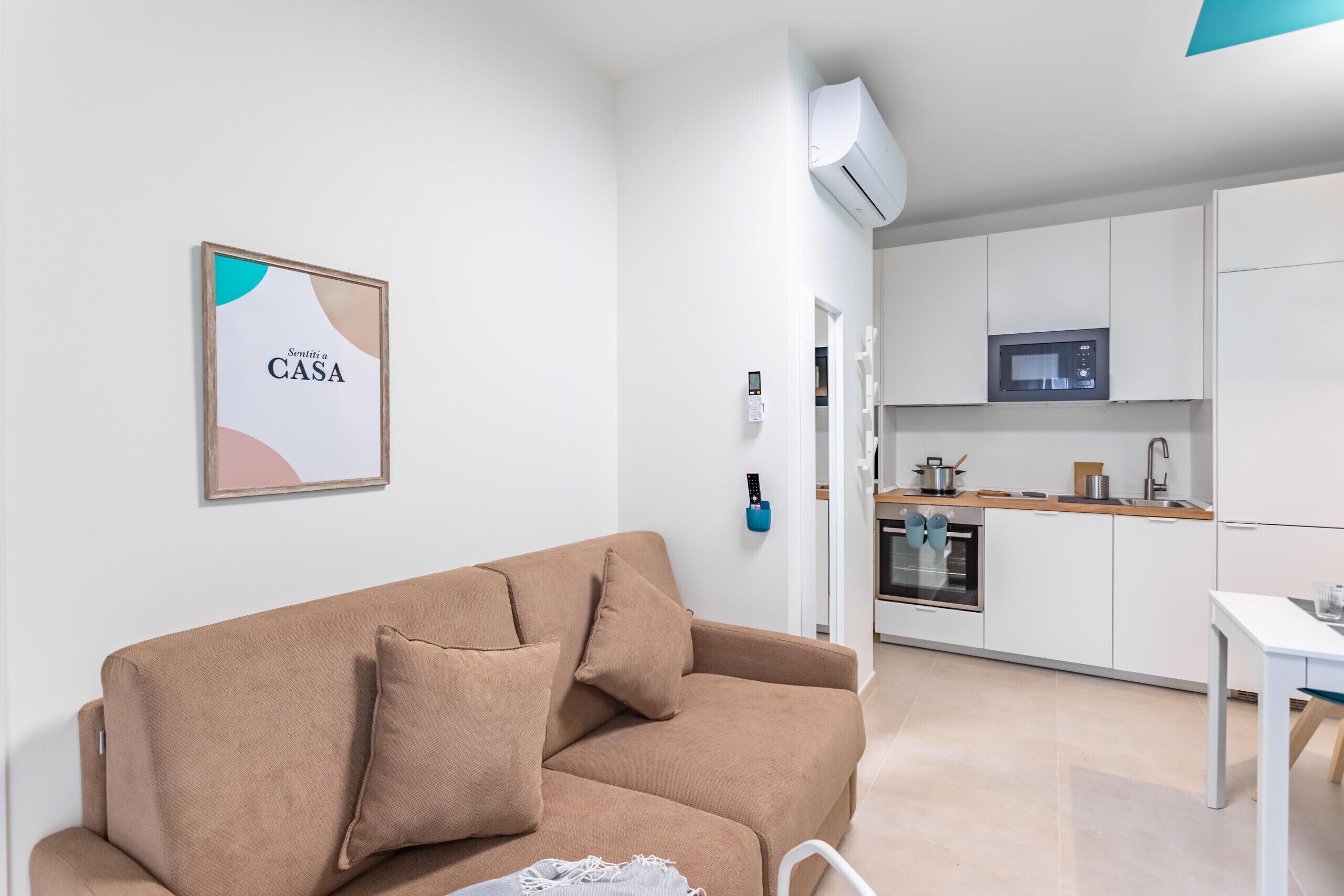 Un salon moderne avec un canapé beige, une petite table et une cuisine en arrière-plan.