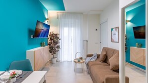 Un salon moderne avec un mur d’accent de couleur turquoise, un canapé beige, un coin repas avec une table dressée et une grande plante en pot.