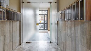 Un couloir bordé de casiers de part et d’autre, avec un sol carrelé et une porte donnant sur un espace extérieur.