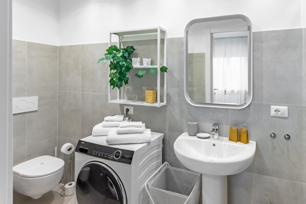 A modern bathroom with a washing machine, a sink, a toilet, and a mirror.