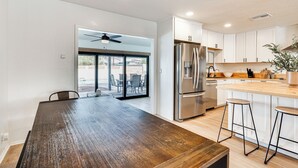 A modern kitchen with white cabinets, stainless steel appliances, and a wooden dining table. - Pool, Grill & Fire Pit: Pet-friendly Arizona Home (Lake Havasu City)