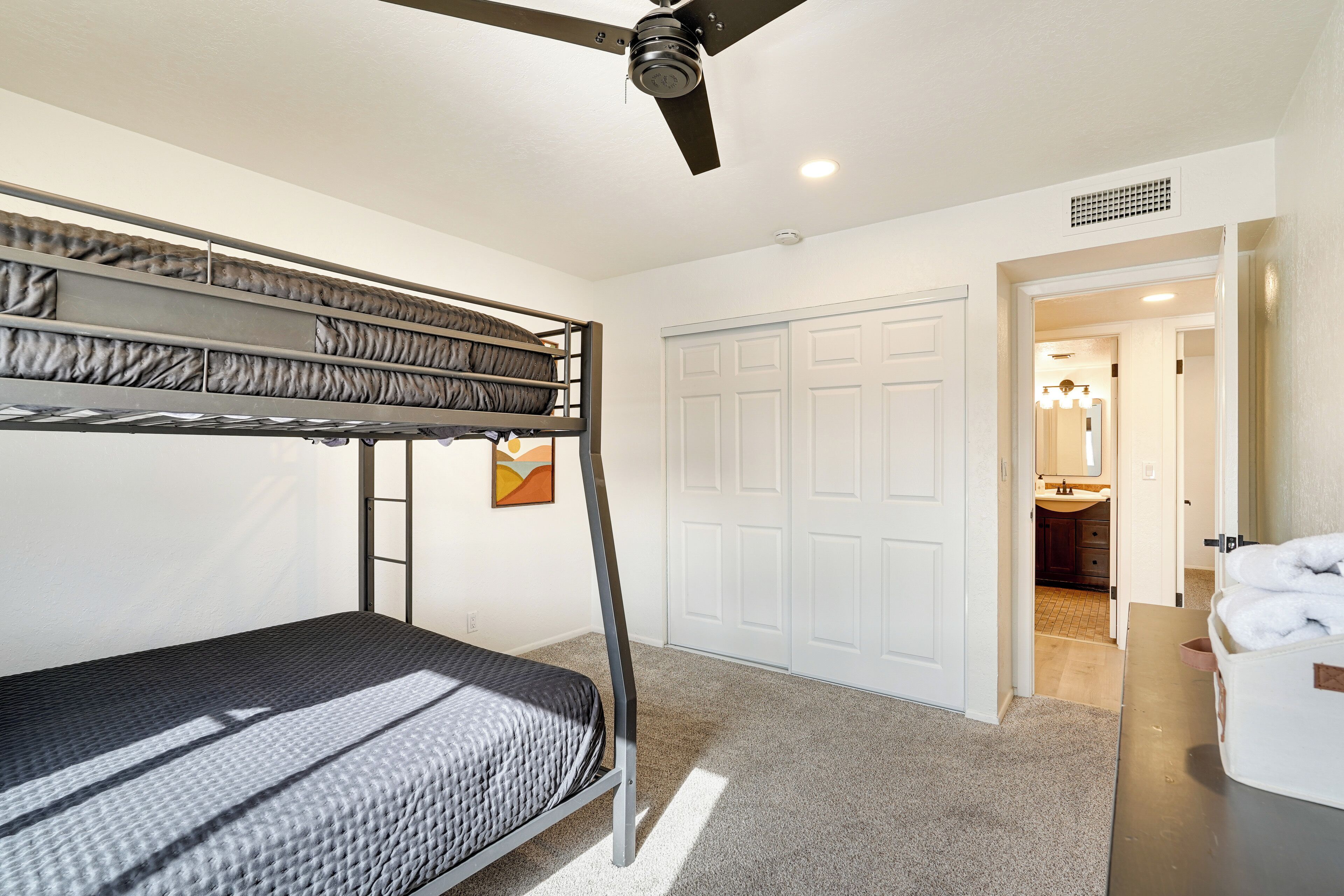 A bunk bed room with a ceiling fan, white closet, and a bathroom visible through an open door.
