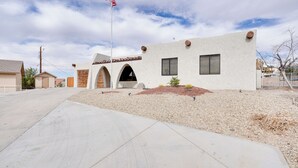 A modern building with a flat roof, a flagpole with an American flag, and a small garden area with a cactus and a birdbath. - Pool, Grill & Fire Pit: Pet-friendly Arizona Home (Lake Havasu City)