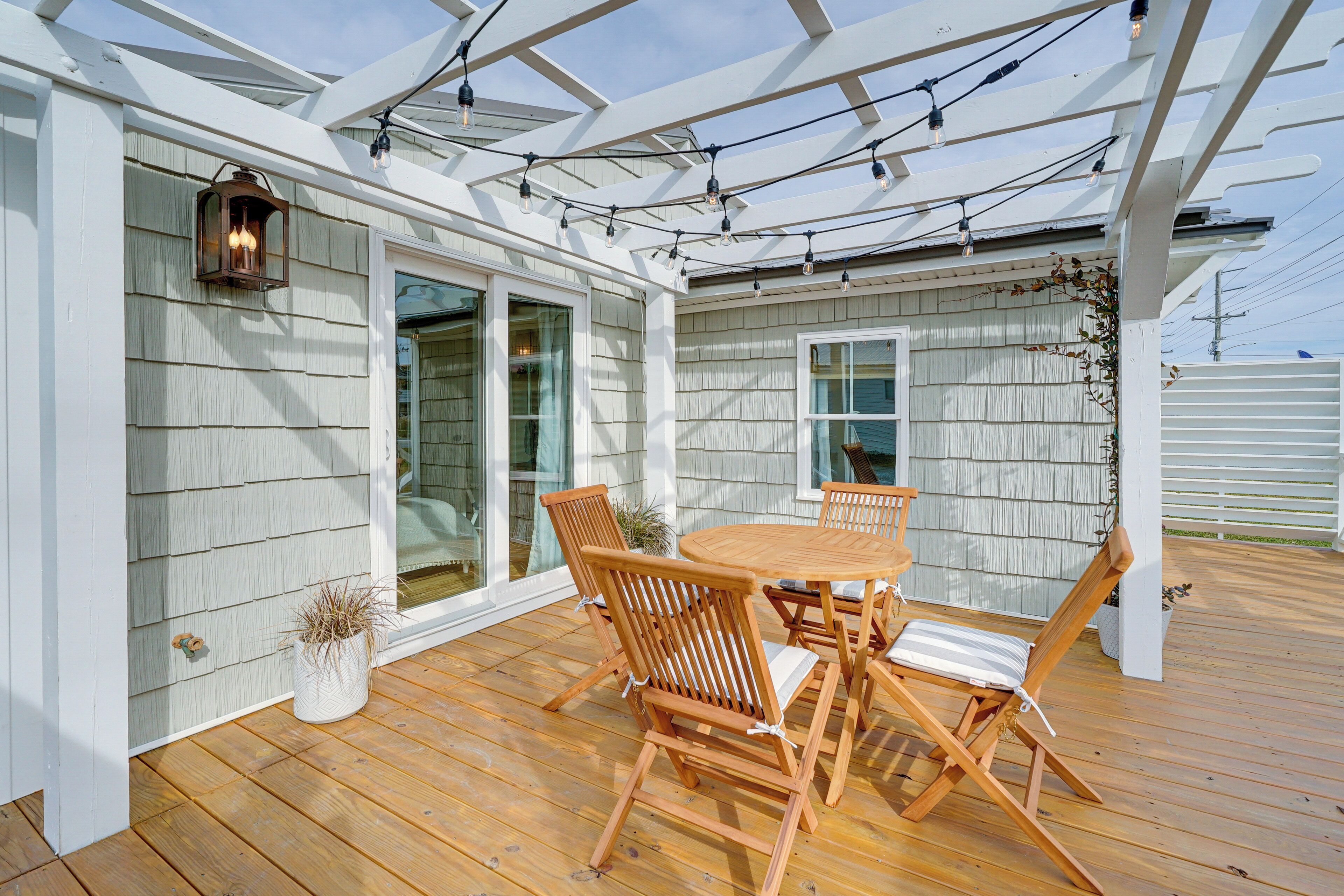 A covered patio with a wooden table and chairs, a lantern, and string lights.