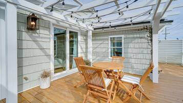 A covered patio with a wooden table and chairs, a lantern, and string lights.