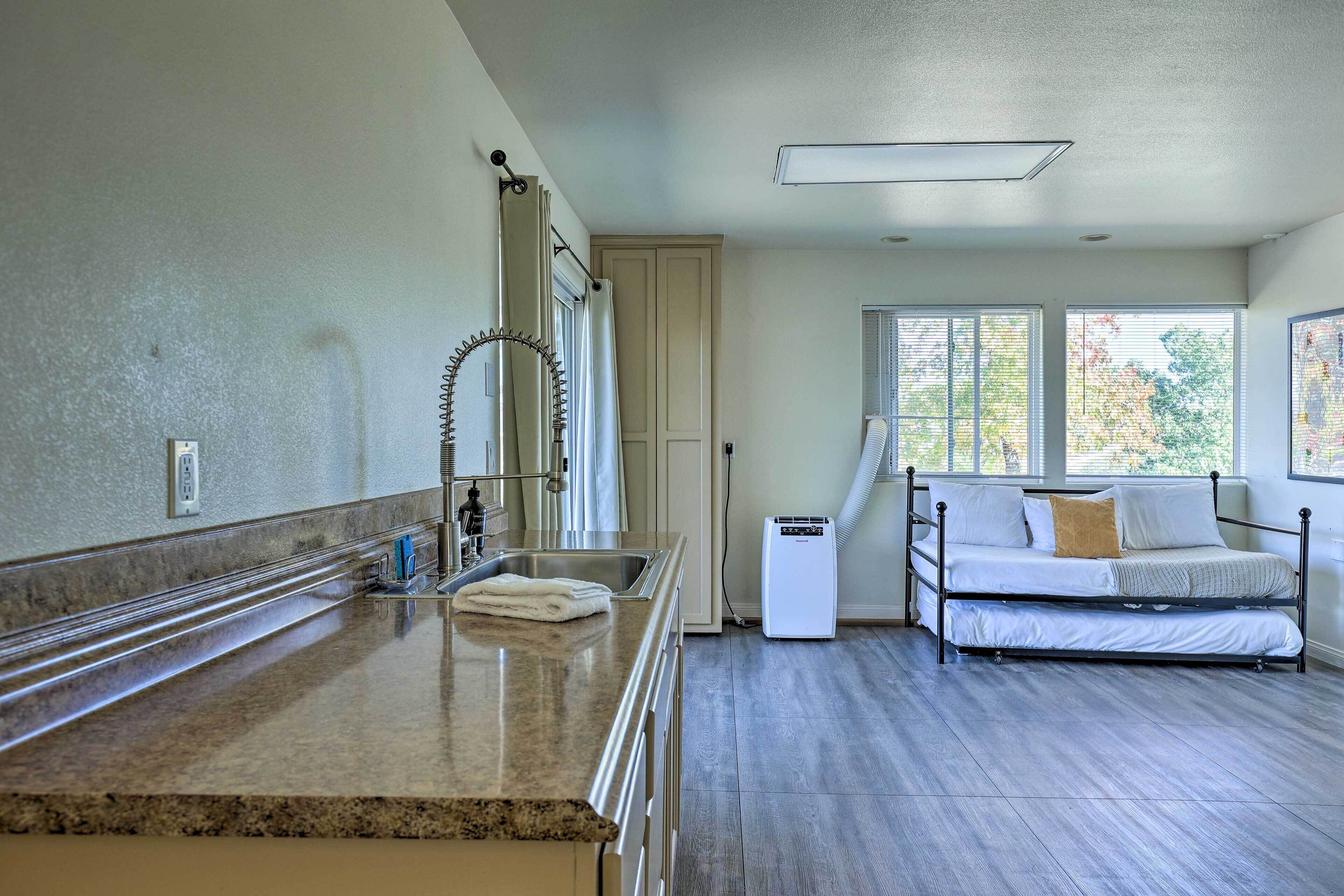 A bedroom with a bed, a window, a heater, and a bathroom with a sink and mirror.