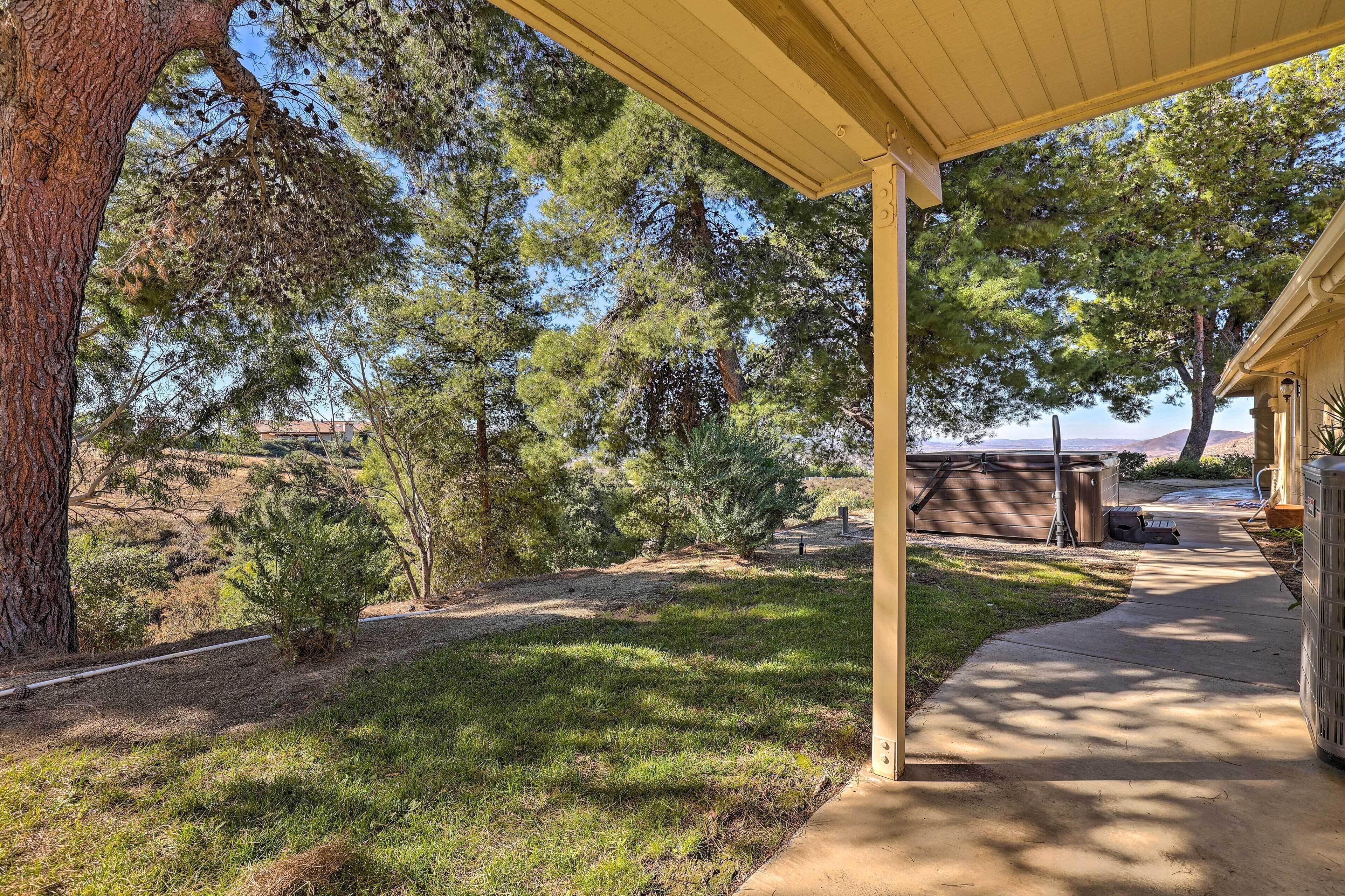 A covered outdoor area with a concrete path, surrounded by trees and a grassy landscape.