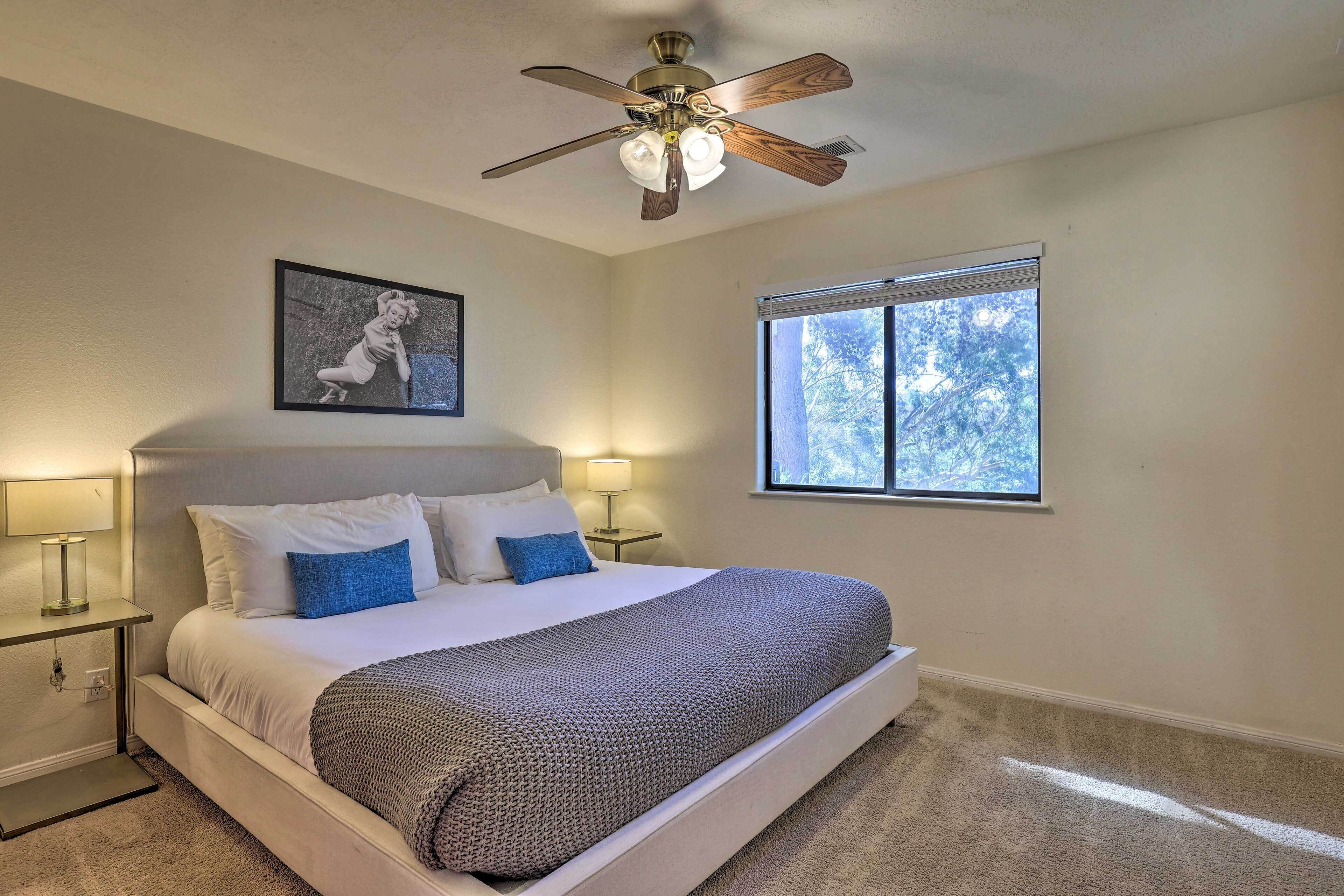 A bedroom with a bed, a ceiling fan, a window, and a nightstand with a lamp.