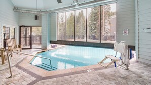 En inomhuspool med utsikt över träd genom stora fönster, en livräddarstol och en poollyft.