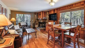 Un salon chaleureux avec une cheminée, des meubles en bois et de grandes fenêtres donnant sur la forêt.